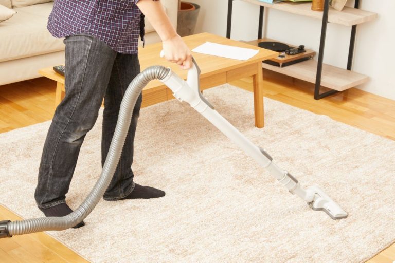 A man using a vacuum cleaner to clean a rug in a well-lit room, focusing on removing dirt and debris.