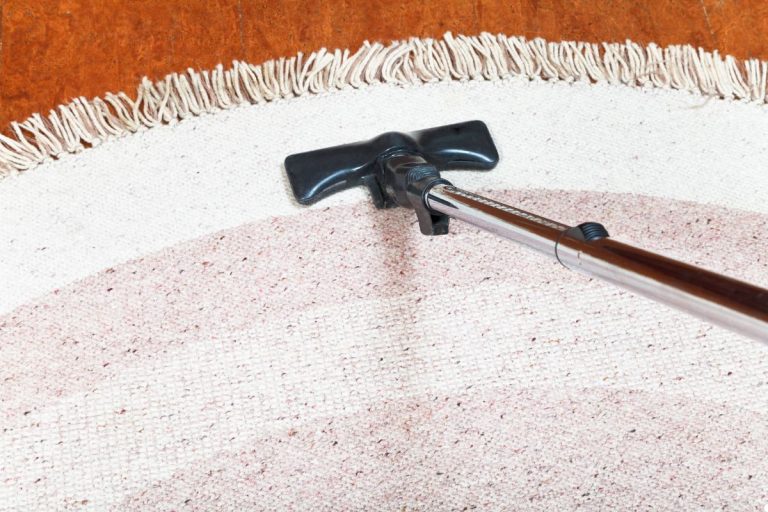 A person vacuuming a rug, focused on removing dirt and debris for a clean living space.